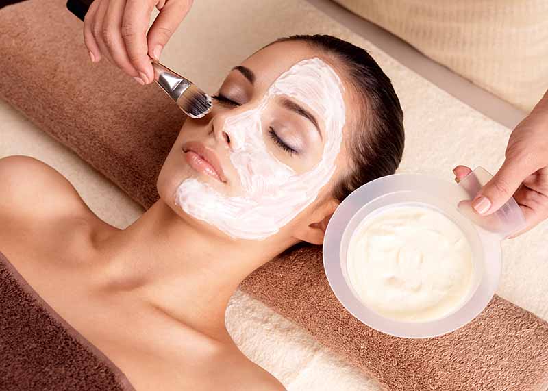 Spa therapy for young woman receiving facial mask at beauty salon - indoors